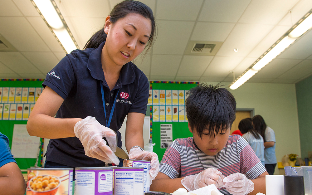 Cedars-Sinai volunteer opening a can with a young boy.