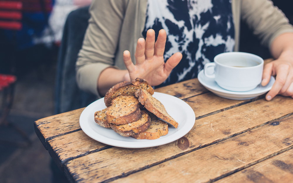 Hand gesturing "no" towards plate of bread.