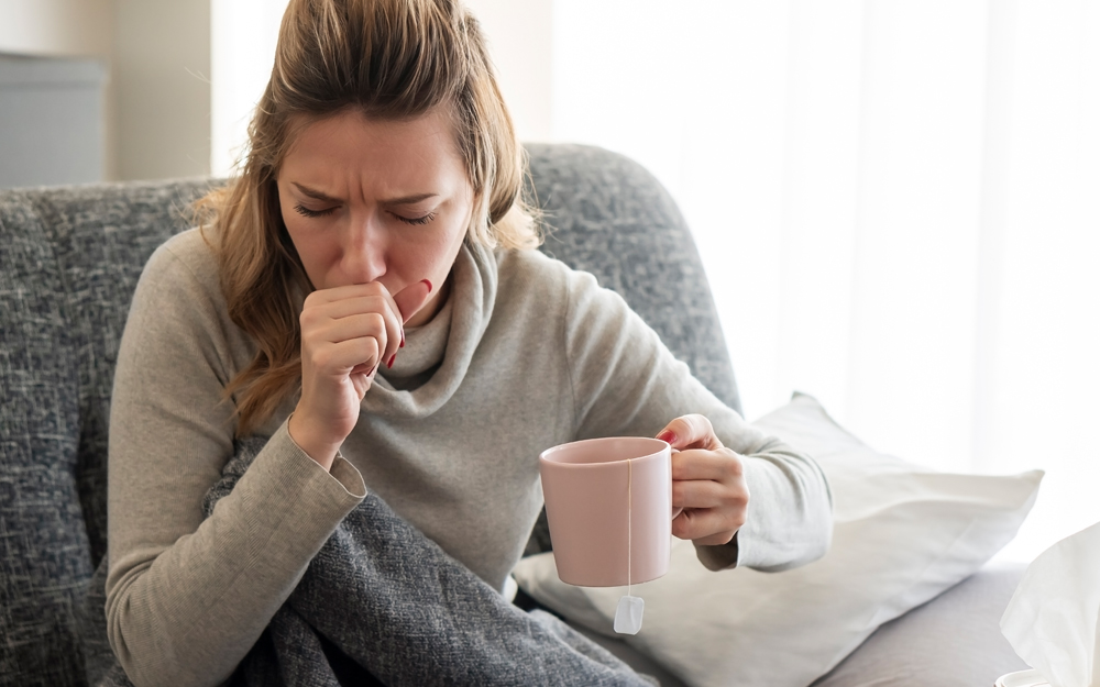 Woman coughing and holding a cup of tea.