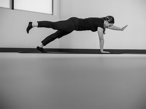 Woman performing a plank, on hands and toes, raise one arm and the opposite leg. 